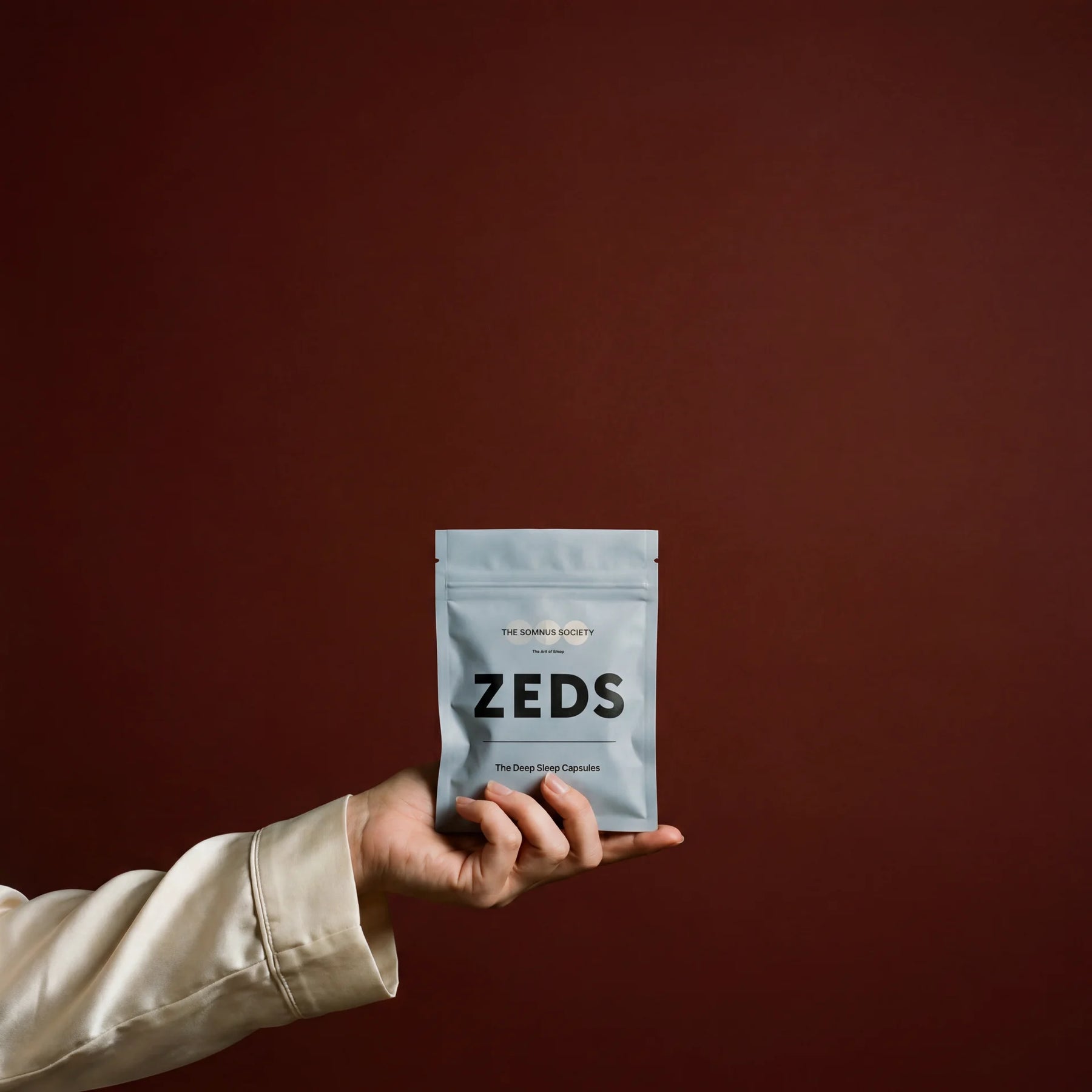 A hand holding the ZEDS sleep capsule pack against an oxblood background